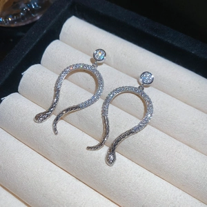 Macro shot of silver snake earrings with full pave cubic zirconia on beige velvet