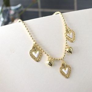 Macro shot of gold beaded chain with white enamel sacred heart pendant and golden charm