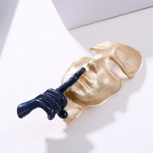 Artistic gold face mask sculpture with deep blue finger silence gesture brooch