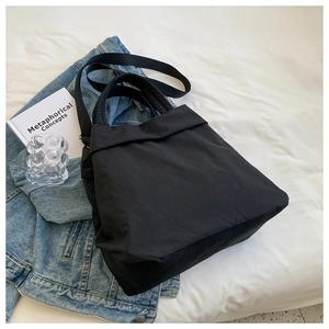Flat lay of a black lightweight nylon tote bag with denim jacket on white bedsheet