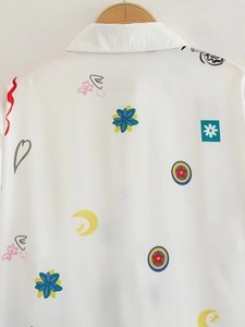 Détail d'une chemise blanche avec motifs graffiti colorés, fleurs et lunes imprimées