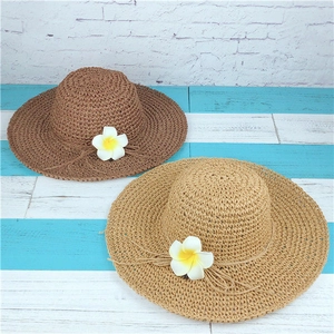 Detail view of woven straw hats in brown and khaki with white plumeria flower and bow
