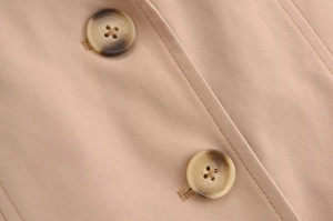 Dettaglio dei bottoni in finta tartaruga sul gilet in twill beige e trama del tessuto