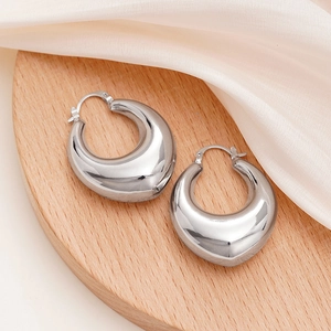 Close-up of chunky silver hoop earrings on a wooden display tray with satin fabric