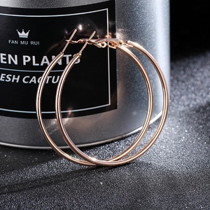 Macro shot of large rose gold thin hoop earrings displayed next to a metal tin