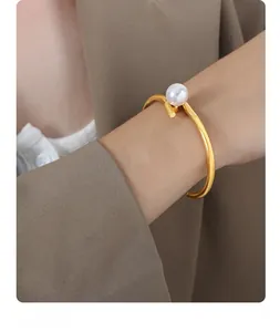 Detailed view of a gold-plated pearl open bangle worn on a model's wrist with a blazer