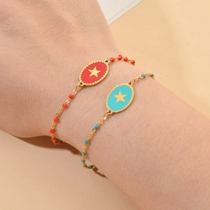 Close-up of red and blue enamel star charms on gold beaded bracelets worn on the wrist
