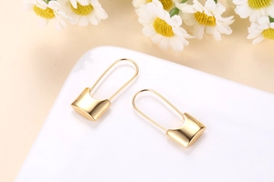 Detail of 18k gold plated safety pin earrings on a white tray with flowers