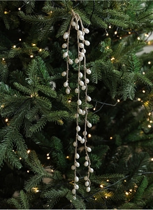 Close-up of white pearl bead garland on a green Christmas tree with warm fairy lights