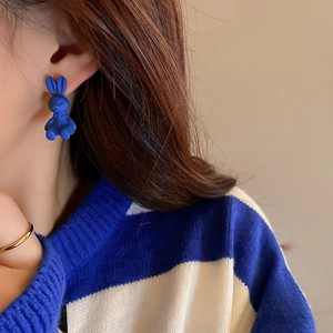Close-up of a model wearing matte blue rabbit stud earrings with striped sweater