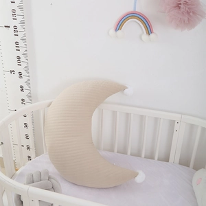 Detailed view of khaki quilted cotton moon nursing pillow with white pom-poms in crib