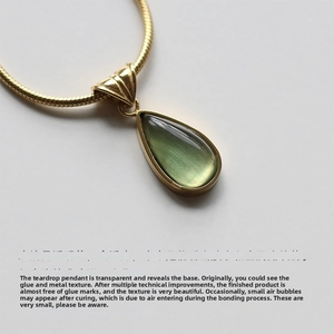 Detail of translucent green teardrop pendant on elegant gold-plated snake chain necklace