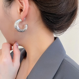 Macro view of minimalist high-polished silver hoop earrings worn on a model's ear