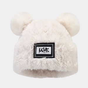 Détail du bonnet en peluche blanc avec écusson Love et pompons doux en fausse fourrure