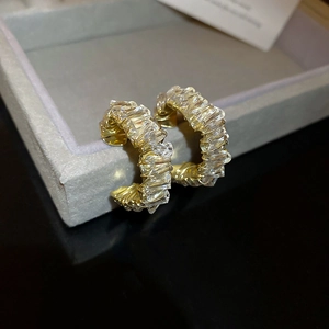 Detailed close-up of golden C-shaped hoop earrings with baguette-cut crystal inlay