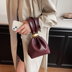 Chic burgundy pleated bucket bag with gold spherical handle shown with trench coat