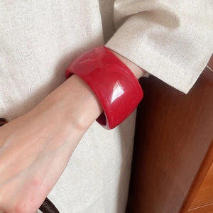 Detail shot of a wide red resin bangle with marble texture on a woman's wrist
