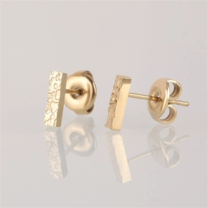 Detailed close-up of golden bar earrings featuring a unique hammered metal texture surface