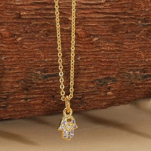 Detailed shot of golden Hamsa Hand pendant with purple gems on a textured wood background