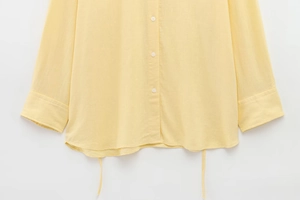 Detail of light yellow long sleeve shirt showing fabric texture and curved hem with drawstrings