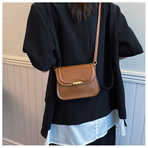 Petit sac bandoulière marron en cuir avec fermoir doré porté par un mannequin