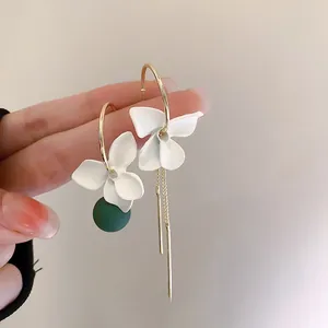 Close-up of asymmetric flower earrings with white petals and gold tassels on fingertips