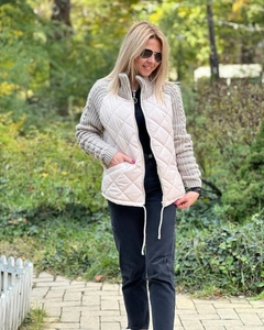 Detail of zip-up quilted jacket with knit sleeves and stand collar in beige color