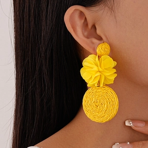 Close-up of yellow fabric flower earrings with woven raffia circles on female model