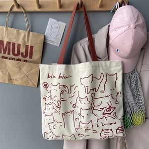Close-up of cream canvas tote bag featuring artistic red cat illustrations and strap
