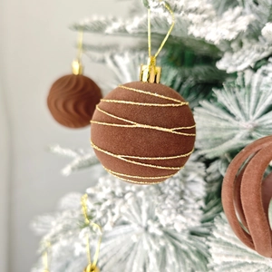 Détail de boules de Noël en velours marron avec lignes dorées sur sapin enneigé