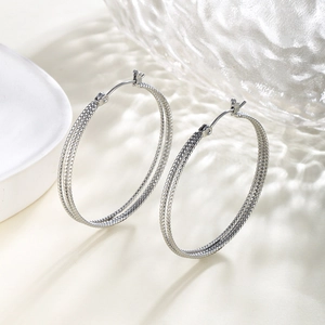 Macro detail of silver-toned hoop earrings with triple layered bead-texture design