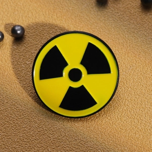 Close-up of yellow radioactive sign enamel pin on textured fabric with metal beads