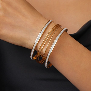 Detail of layered gold geometric bracelets featuring textured and faceted finishes on wrist