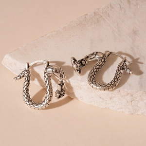 Macro shot of silver snake earrings with orb pendant on a textured stone display