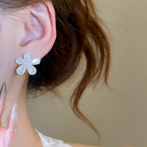 Close-up of five-petal flower stud earring with shimmering zircons and a central pearl
