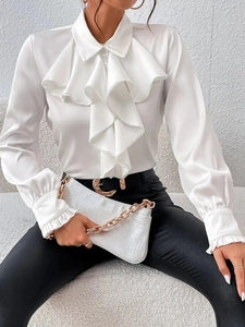 Dettaglio di un'elegante camicia in raso bianco con volant e polsini svasati da donna
