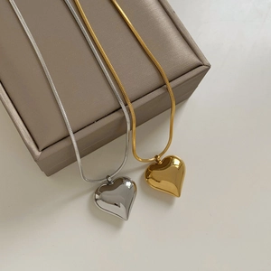 Minimalist gold and silver heart pendant necklaces with square snake chain on a beige surface