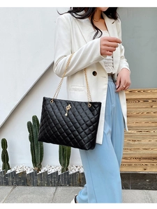 Close-up of black quilted tote bag with gold chain strap and crown charm pendant