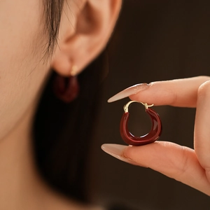 Close-up of deep red U-shaped earrings with gold plating worn and held to show detail