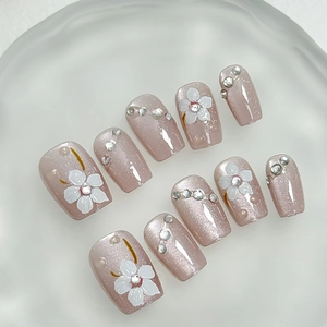 Handmade cat-eye press-on nails with white flowers and pearls on a round tray