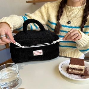 Detailed view of black plush cosmetic bag showing zipper opening and soft fuzzy texture