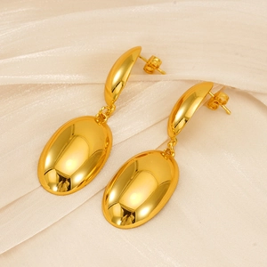 Détail de boucles d'oreilles ovales dorées avec fini miroir sur tissu en soie crème