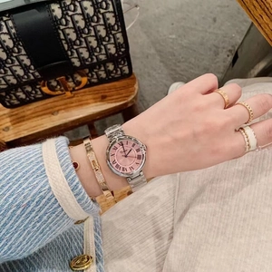 Close-up of silver watch with pink dial and Roman numerals, styled with fashion jewelry