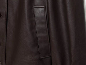 Detailed close-up of stitching and pocket flap on dark brown textured leather jacket