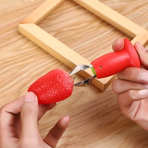 Close-up of hand using a red strawberry huller to remove stems on a wooden background