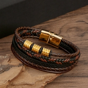 Detail of woven brown and black leather bracelet with gold metal rings on wood