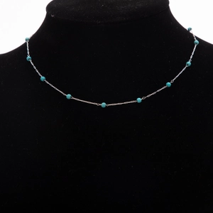 Détail de chaîne argentée avec perles bleu ciel sur présentoir noir