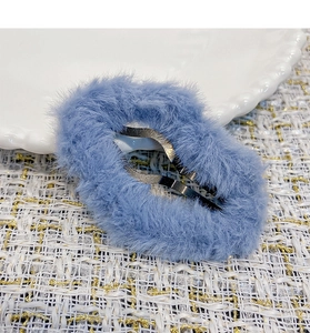 Close-up of a blue plush oval BB hair clip on a white ceramic plate with textured fabric