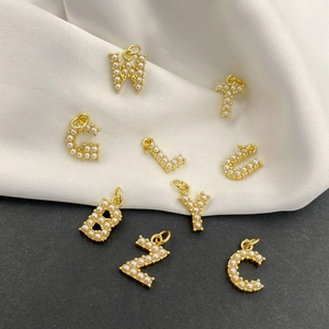 Close-up of gold alphabet pendants with pearl inlay on white silk fabric background