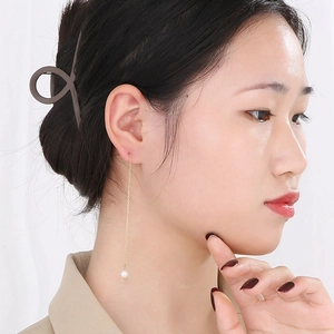 Détail d'une boucle d'oreille longue chaîne à pompon doré avec perle blanche sur modèle